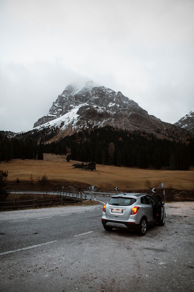 Lonely road with car on roadside among pine forest near big cliffs