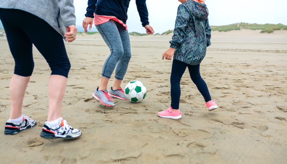 Three female generations playing soccer on the beach