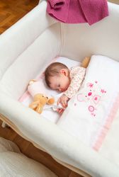 Baby girl sleeping in a white cot with pacifier and toy
