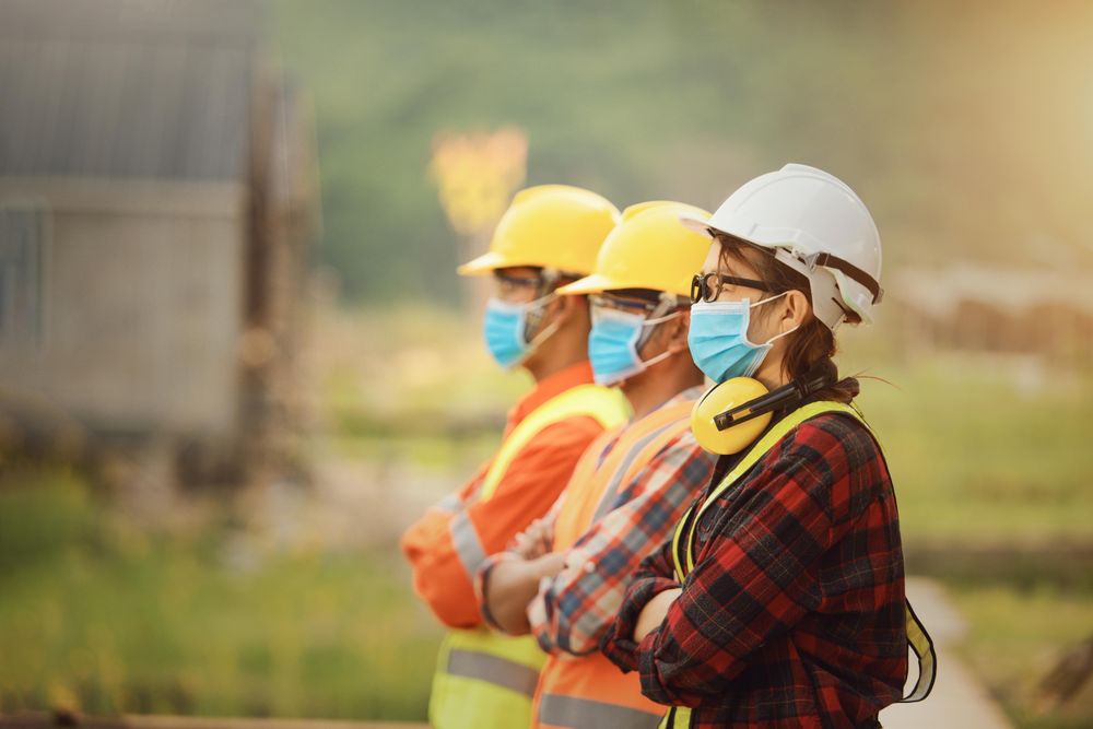 Female architect and two men in bump caps and facemask standing looking away