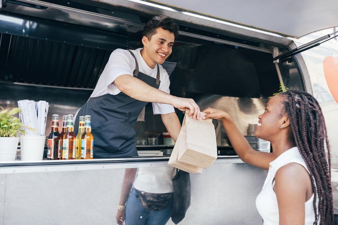 Woman picking up meal in two paper bags from smiling vendor