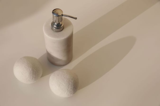 Dryer wool balls and luxury marble stone soap dispenser bottle on blurred beige table background in sunlight. Long soft shadows. Hygiene, bodycare laundry or bathroom concept. High angle view