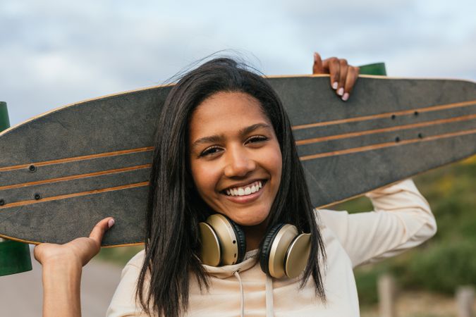 Joyful woman standing with longboard behind head