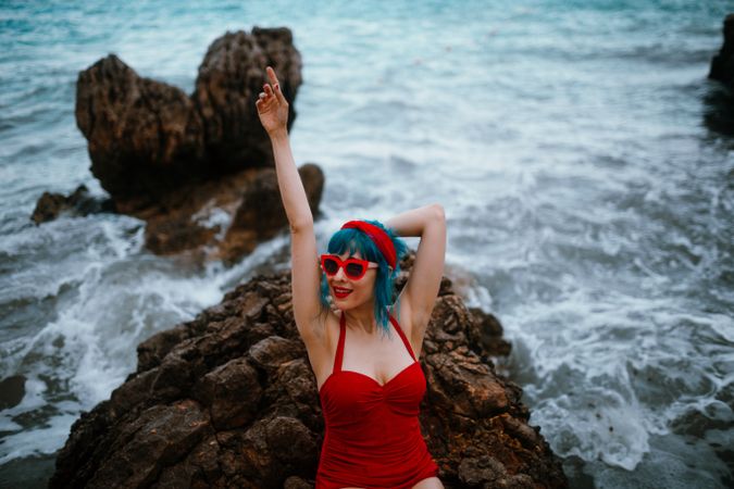 Graceful woman with trendy hairstyle tanning on rocky stone in water