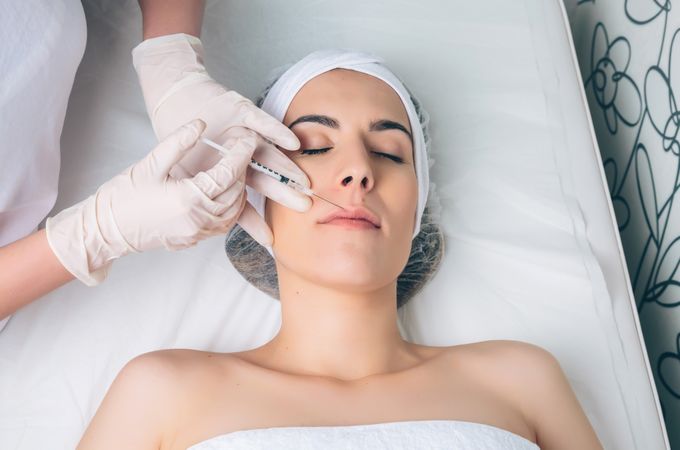 Aesthetician's hand's in latex gloves injecting filler into female's lips in a beauty salon