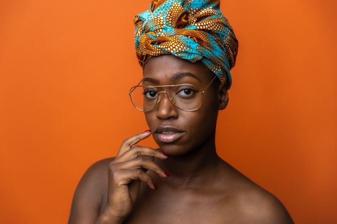 Portrait of Black woman with eyeglasses wearing African headwrap against orange background
