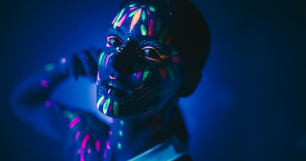 Beauty Close Up Photo: Young Female Poses with Confidence, Neon Paint Accentuating Her Facial Features Against an Low Key Studio Setting, Creating an Artistic Appearance