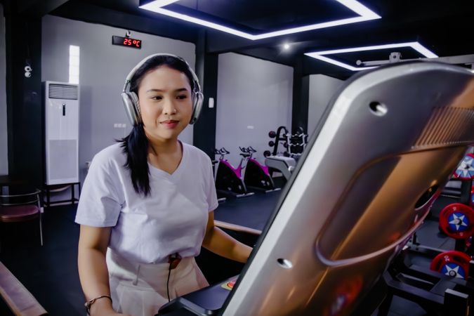 Asian woman on treadmill enjoys music using headphones in g