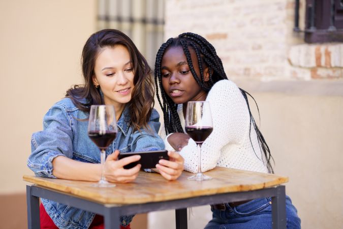 Female friends looking at phone screen at a restaurant with red wine