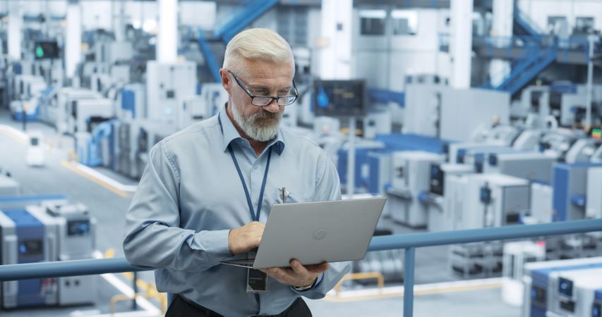 Mature Engineer Monitoring and Analyzing Conditions at an Automated Modern Electronics Factory with Mobility Robots Working with the Help of Artificial Intelligence Software