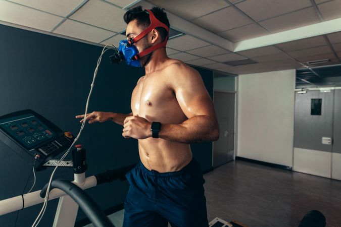 Muscular man with face mask for feedback running on treadmill in gym