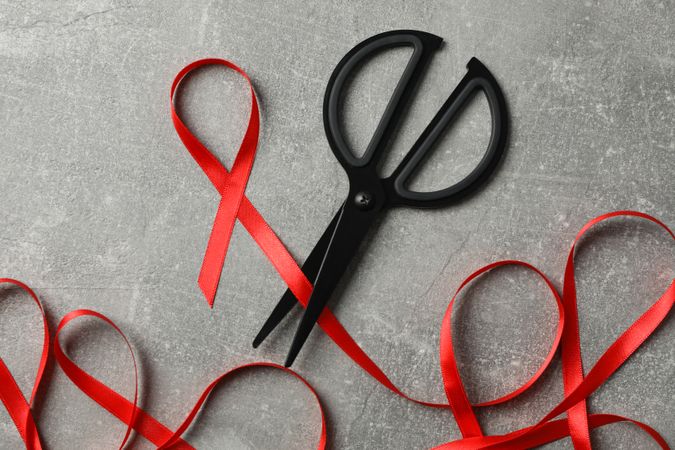 Awareness red ribbon and scissors on grey background, copy space