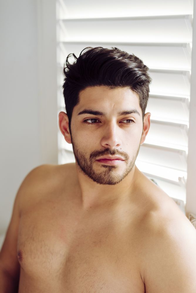 Young cheerful naked man leaning on window