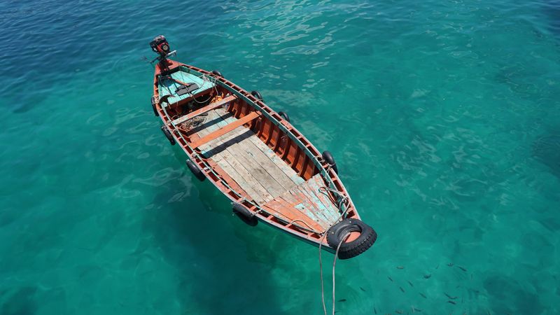 A small boat in the middle of the blue ocean surrounded by a school of fish.