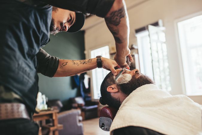Barber shaving man’s face in barbershop