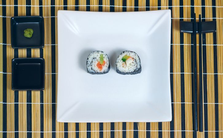 Top view of sushi maki rolls presented on a plate with sauces and chopsticks