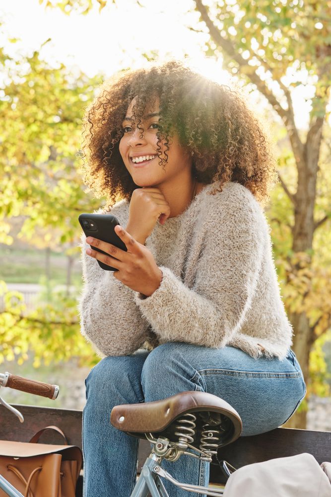 Smiling Hispanic woman resting on bench with cellphone