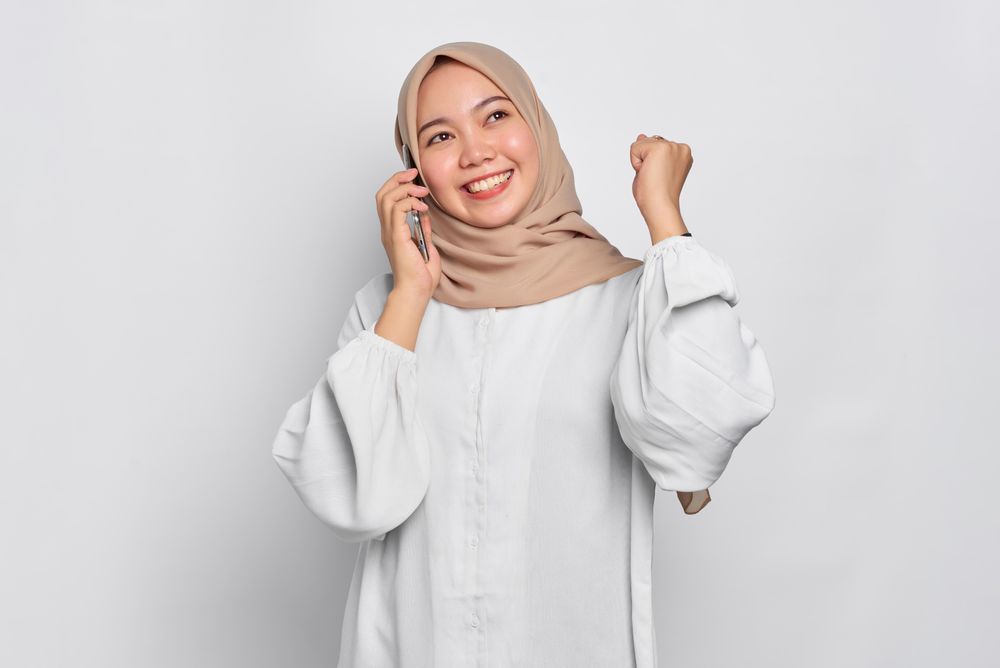 Asian Muslim woman celebrating good news being received through her cell phone
