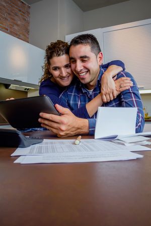 Smiling couple holding each other as they organize bills together in their kitchen