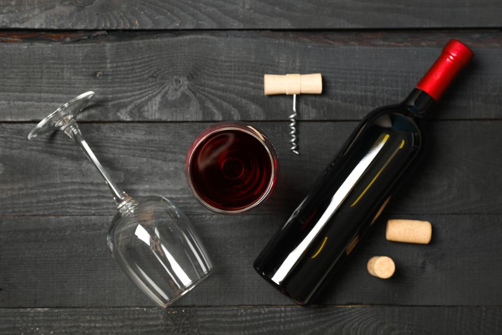 Flat lay composition with bottle of wine, glasses and corkscrew on wooden background, copy space
