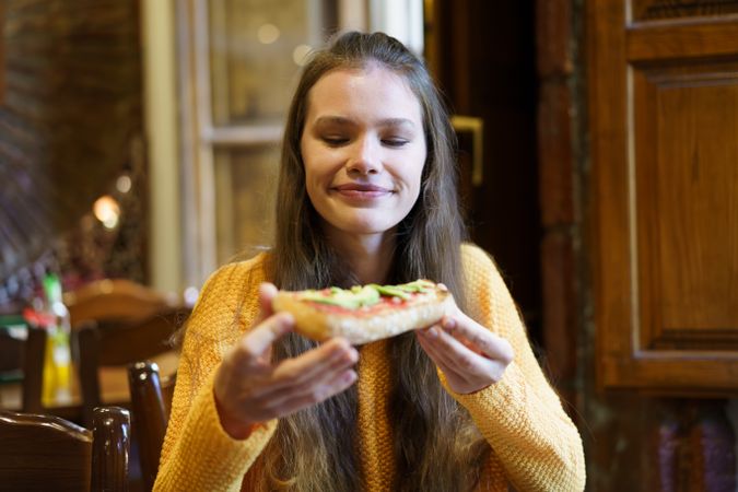 Joyful Young Woman Happily Enjoying a Deliciously Savory Slice of Pizza in a Cozy Restaurant Setting