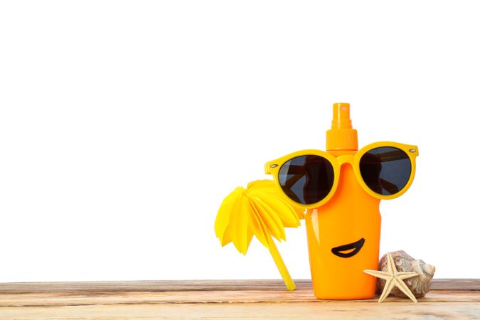 Sunscreen spray with sunglasses, starfish, seashell and decorative palm on wooden table, isolated on neutral background. Safe tan