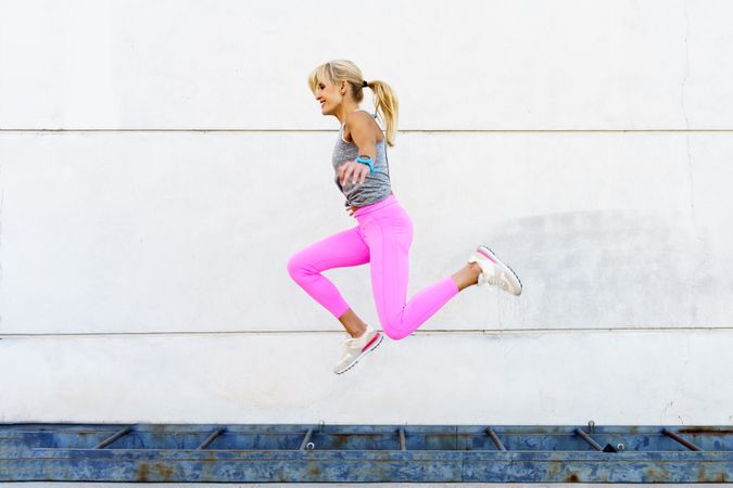 Fit woman in pink leggings doing jumps outside