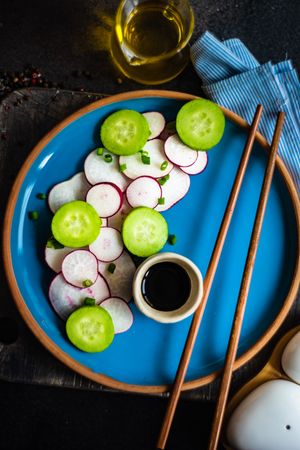 Top view of sliced radishes and cucumber on blue plate