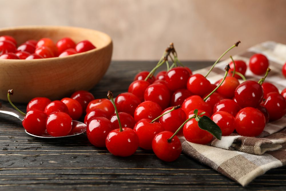 Towel, spoon and bowl with cherry on wooden background, close up