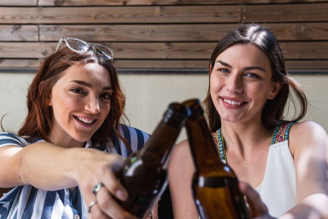 Cheerful girlfriends with beer spending weekend on sofa