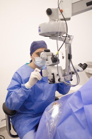 Doctor looking through eye equipment at patient in cataract surgery, vertical