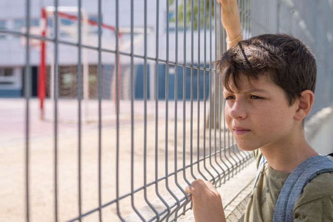 Boy holding gate looking wistfully into school yard