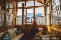 Woman sitting on  armchair looking at mountains through the window 0Jyqnb