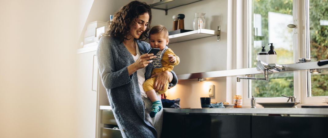 Working mother on maternity leave carrying baby and looking at smart phone