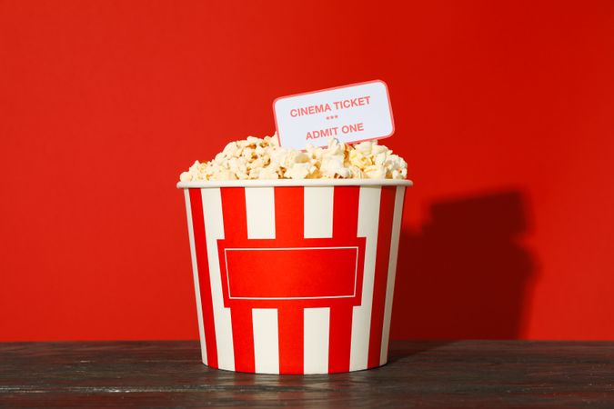 Striped bucket with popcorn and tickets against red background