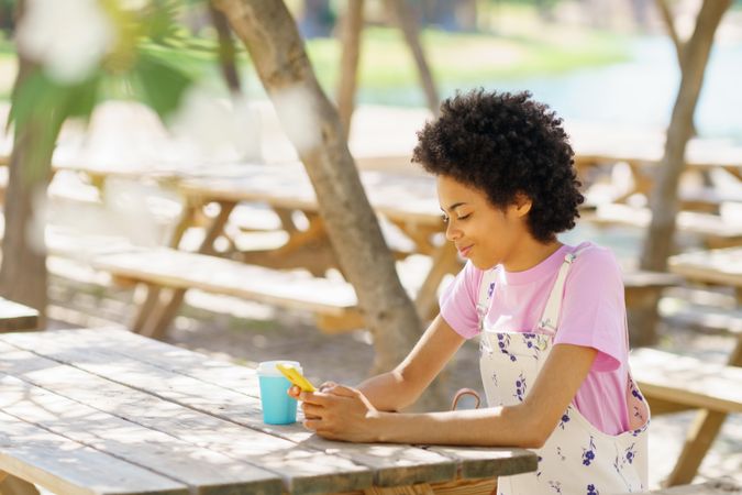 Smirking woman sitting on park table texting