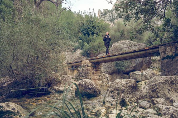 Young traveling woman walking on footbridge during hiking in woo
