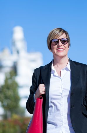 Professional woman walking outside with sunglasses and red bag