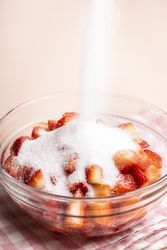 Pouring sugar over sliced strawberries for pie