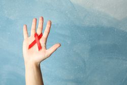 Hand and red awareness ribbon against blue background, space for text