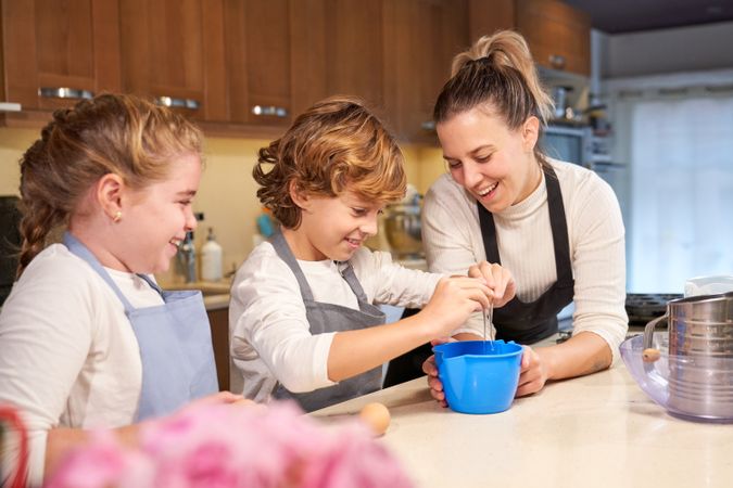 Cheerful kids cooking dough together with mother