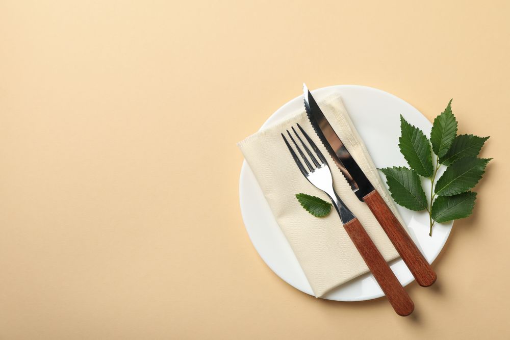 Plate with napkin, cutlery and leaf on beige background, top view
