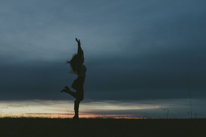 Side view of  woman dancing in a field at dusk