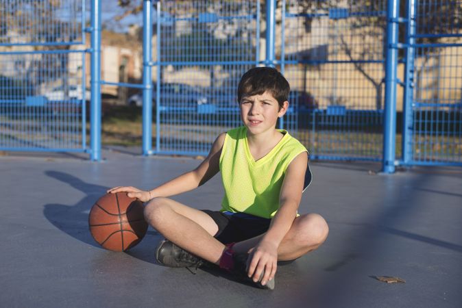 Young basketball player sitting on the court wearing a yellow sleeveless shirt