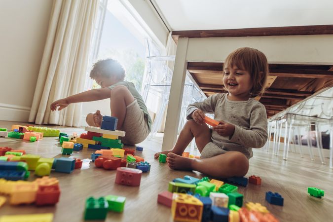 Happy brothers playing with building blocks sitting on floor
