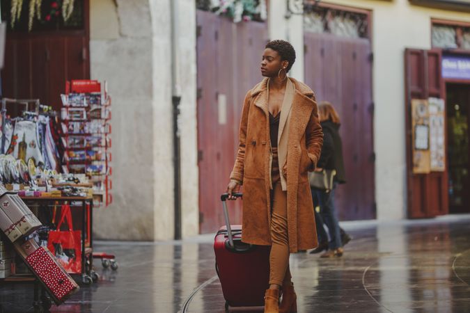 Stylish Black woman with luggage walking on street