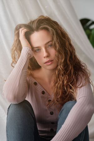 Charming woman sitting near curtain and daydreaming
