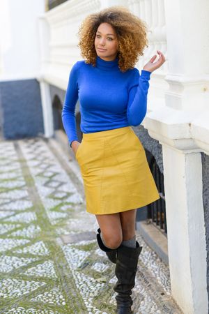 Nonchalant female with curly hair and boots wearing bright clothes pictured in courtyard