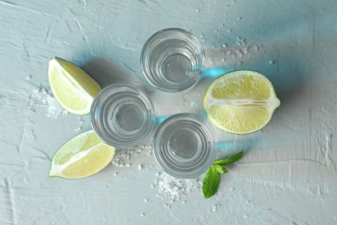 Tequila shots, salt, lime slices and mint on cement background