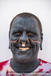 Man smiling with extreme body modification, full face tattoos and multiple gauge piercings 0KMNN4